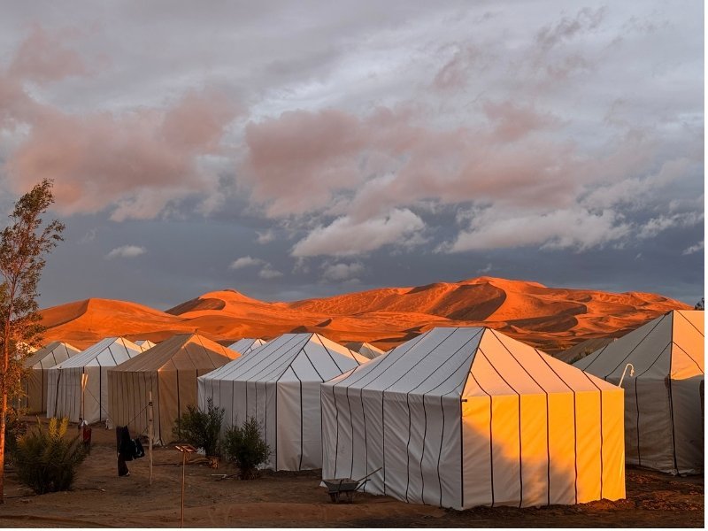 White luxury tents at Merzouga Luxury Camp beneath a colorful Sahara sunset.